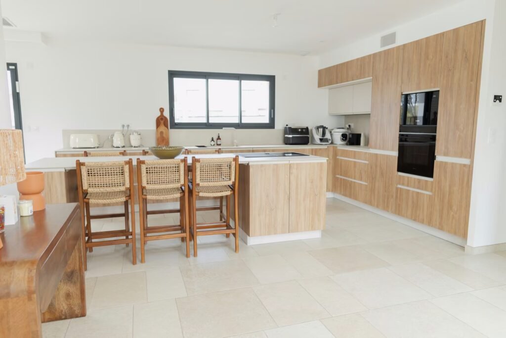 Cuisine moderne rénovée à Ingré avec meubles en bois clair, îlot central blanc, sol carrelé et électroménager encastré