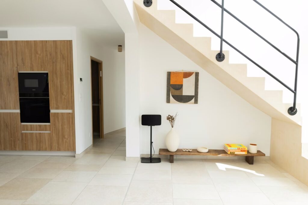 Entrée intérieure rénovée avec escalier blanc, garde-corps noir, sol carrelé clair et décoration sous escalier