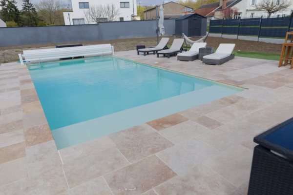 Piscine extérieure avec plage en dalles claires, margelles ton pierre, transats et jardin clôturé