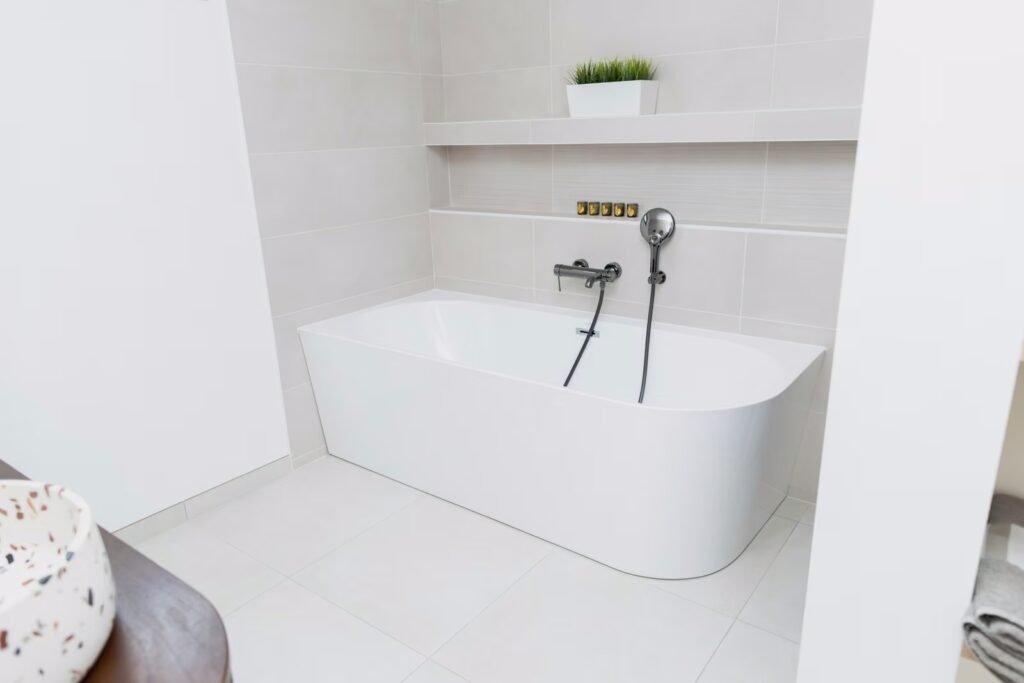 Salle de bains rénovée avec baignoire blanche, robinetterie murale, faïence claire et tablette décorative