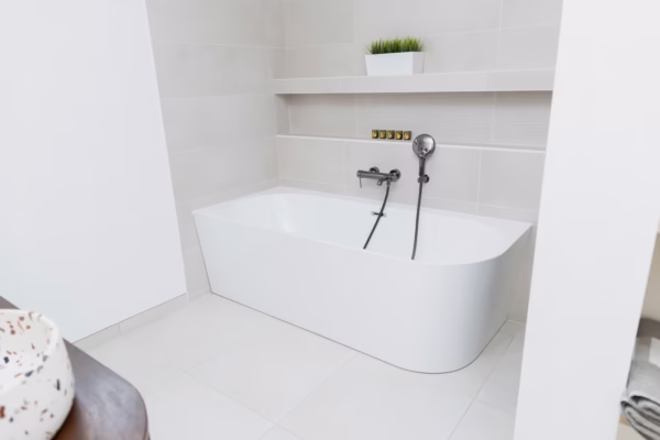 Salle de bains rénovée avec baignoire blanche, robinetterie murale, faïence claire et tablette décorative