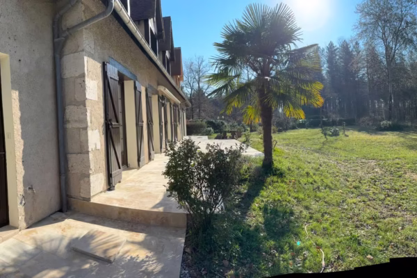 Terrasse extérieure rénovée en pierre claire le long d’une maison avec façade ancienne, jardin et pelouse