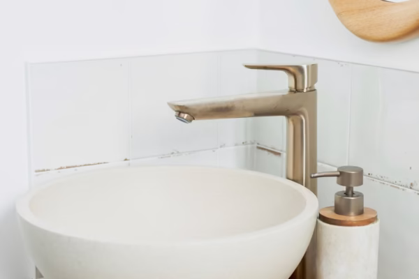 WC rénové avec lave-mains rond blanc, meuble bois à lattes, robinetterie murale dorée et miroir arrondi